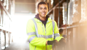 Image shows a man wearing a yellow caution vest and smiling while working in a warehouse.